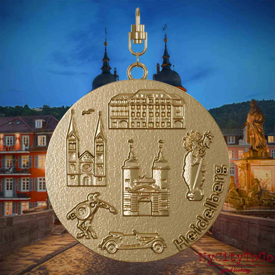 Halskette mit Drehwirbel und Rückseite eines Schmuckanhängers aus vergoldetem Edelstahl, auf dem Reliefs bekannter Sehenswürdigkeiten der Stadt Heidelberg abgebildet sind. Den Hintergrund bildet eine Ansicht der Stadt Heidelberg .

