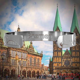 Innenseite eines silbernen Armreifs mit Reliefs bekannter Sehenswürdigkeiten der Stadt Bremen und einer Gravur des Stadtnamens. Den Hintergrund bildet eine Ansicht der Stadt Bremen.