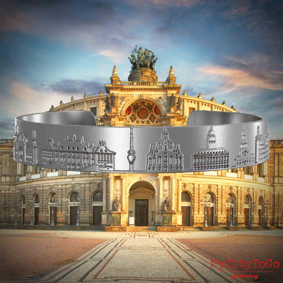 Armreif aus Edelstahl mit Reliefs bekannter Sehenswürdigkeiten der Stadt Dresden. Den Hintergrund bildet eine Ansicht der Stadt Dresden.