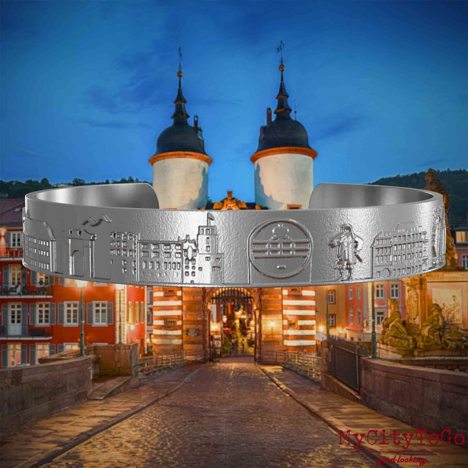 Armreif aus Edelstahl mit Reliefs bekannter Sehenswürdigkeiten der Stadt Heidelberg. Den Hintergrund bildet eine Ansicht der Stadt Heidelberg.
