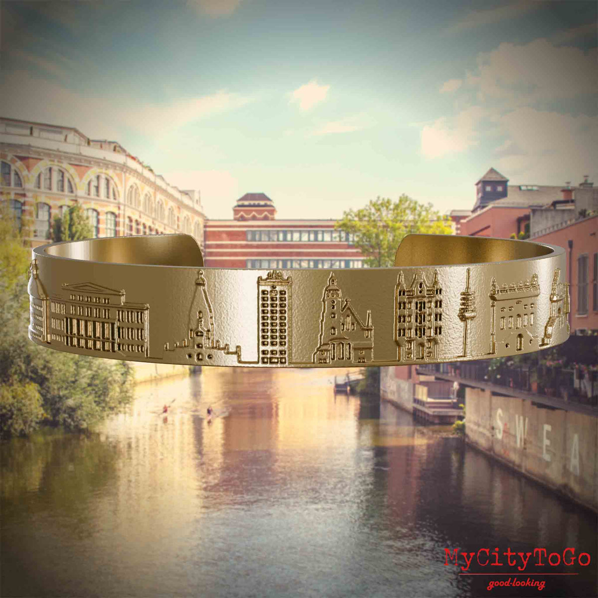 Armreif aus vergoldetem Edelstahl mit Reliefs bekannter Sehenswürdigkeiten der Stad Leipzig. Den Hintergrund bildet eine Ansicht der Stadt Leipzig.