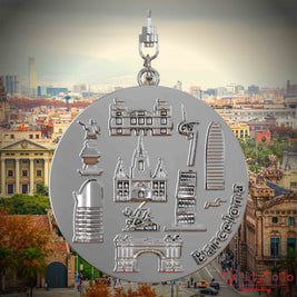 Halskette mit Drehwirbel und Vorderseite eines silbernen Schmuckanhängers, auf dem Reliefs bekannter Sehenswürdigkeiten der Stadt Barcelona abgebildet sind. Den Hintergrund bildet eine Ansicht der Stadt Barcelona.
