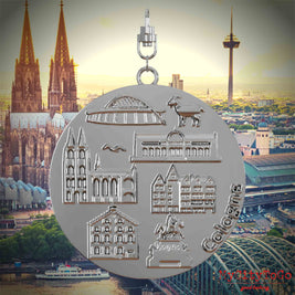Halskette mit Drehwirbel und Vorderseite eines silbernen Schmuckanhängers, auf dem Reliefs bekannter Sehenswürdigkeiten der Stadt Koeln abgebildet sind. Den Hintergrund bildet eine Ansicht der Stadt Koeln.