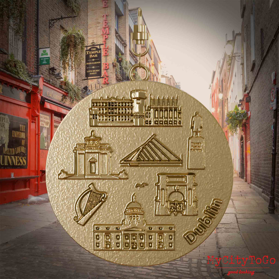 Halskette mit Drehwirbel und Rückseite eines Schmuckanhängers aus vergoldetem Edelstahl, auf dem Reliefs bekannter Sehenswürdigkeiten der Stadt Dublin abgebildet sind. Den Hintergrund bildet eine Ansicht der Stadt Dublin.
