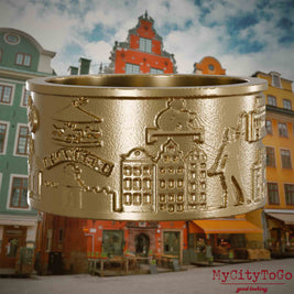 Ring aus vergoldetem Edelstahl mit Reliefs bekannter Sehenswürdigkeiten der Stadt Stockholm. Den Hintergrund bildet eine Ansicht der Stadt Stockholm.