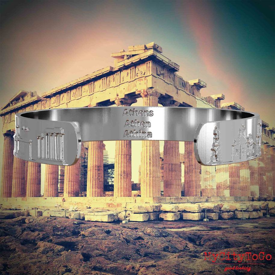 Innenseite eines silbernen Armreifs mit Reliefs bekannter Sehenswürdigkeiten der Stadt Athen und einer Gravur des Stadtnamens. Den Hintergrund bildet eine Ansicht der Stadt Athen.
