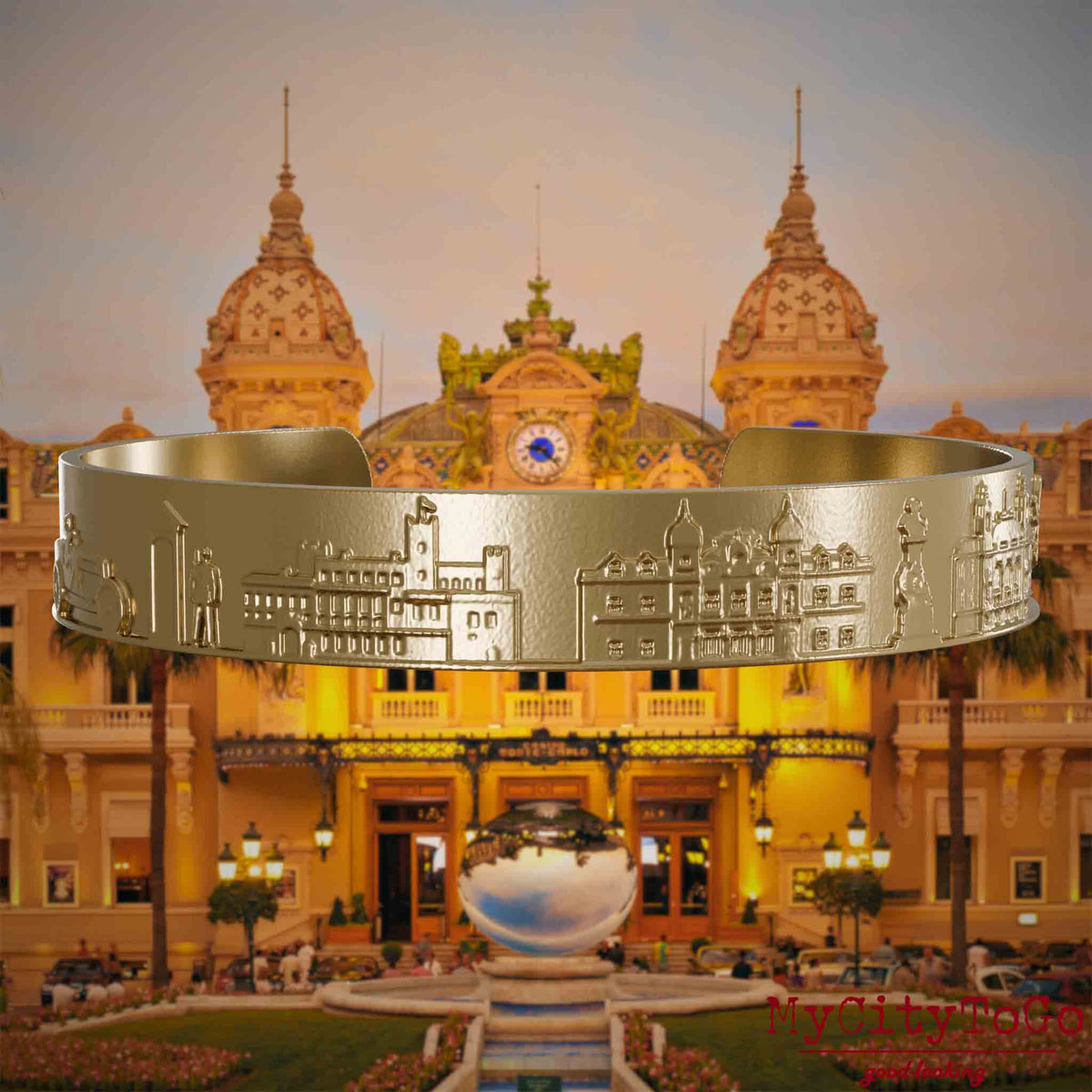 Armreif aus vergoldetem Edelstahl mit Reliefs bekannter Sehenswürdigkeiten der Stadt Monte Carlo. Den Hintergrund bildet eine Ansicht der Stadt Monte Carlo.