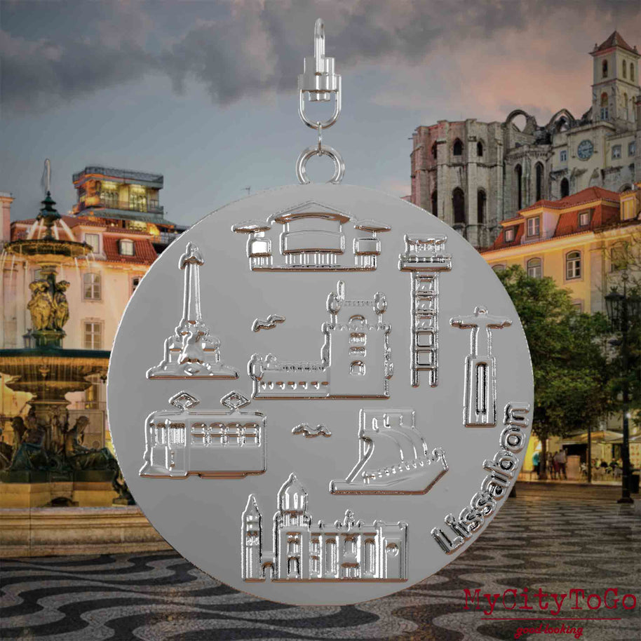 Halskette mit Drehwirbel und Vorderseite eines silbernen Schmuckanhängers, auf dem Reliefs bekannter Sehenswürdigkeiten der Stadt Lissabon abgebildet sind. Den Hintergrund bildet eine Ansicht der Stadt Lissabon.
