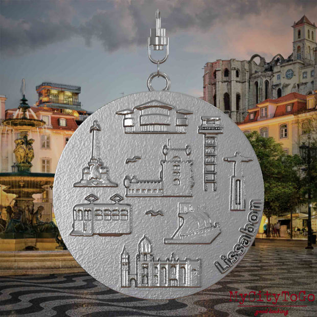 Halskette mit Drehwirbel und Vorderseite eines Schmuckanhängers aus Edelstahl, auf dem Reliefs bekannter Sehenswürdigkeiten der Stadt Lissabon abgebildet sind. Den Hintergrund bildet eine Ansicht der Stadt Lissabon.
