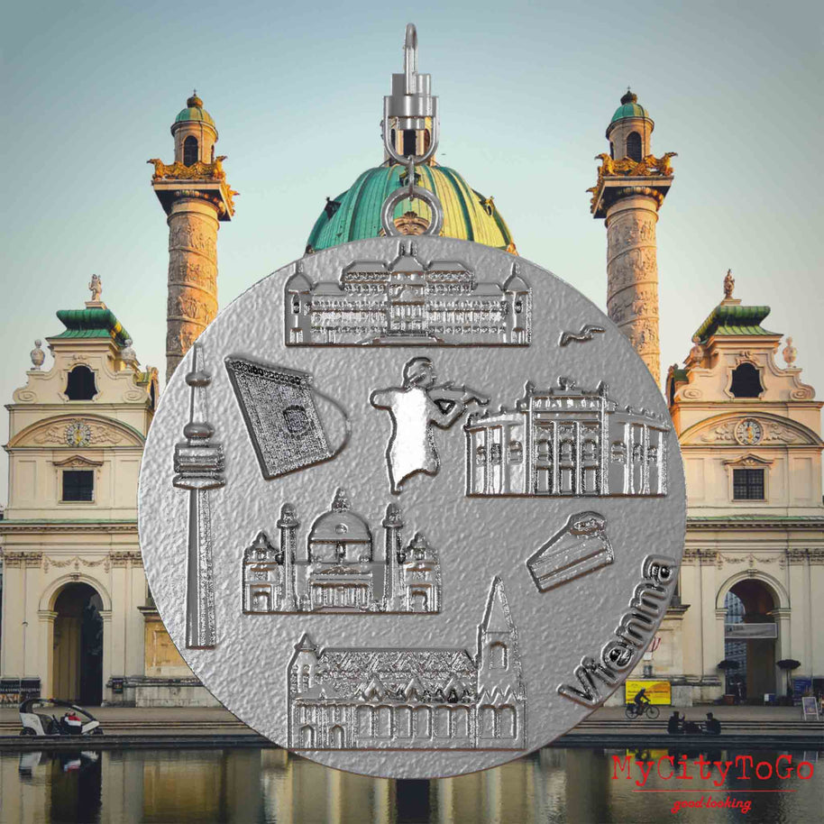 Halskette mit Drehwirbel und Rückseite eines Schmuckanhängers aus Edelstahl, auf dem Reliefs bekannter Sehenswürdigkeiten der Stadt Wien abgebildet sind. Den Hintergrund bildet eine Ansicht der Stadt Wien.
