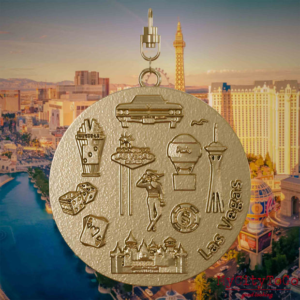 Halskette mit Drehwirbel und Rückseite eines Schmuckanhängers aus vergoldetem Edelstahl, auf dem Reliefs bekannter Sehenswürdigkeiten der Stadt Las Vegas  abgebildet sind. Den Hintergrund bildet eine Ansicht der Stadt Las Vegas.
