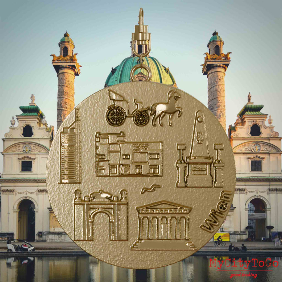 Halskette mit Drehwirbel und Vorderseite eines Schmuckanhängers aus vergoldetem Edelstahl, auf dem Reliefs bekannter Sehenswürdigkeiten der Stadt Wien abgebildet sind. Den Hintergrund bildet eine Ansicht der Stadt Wien.
