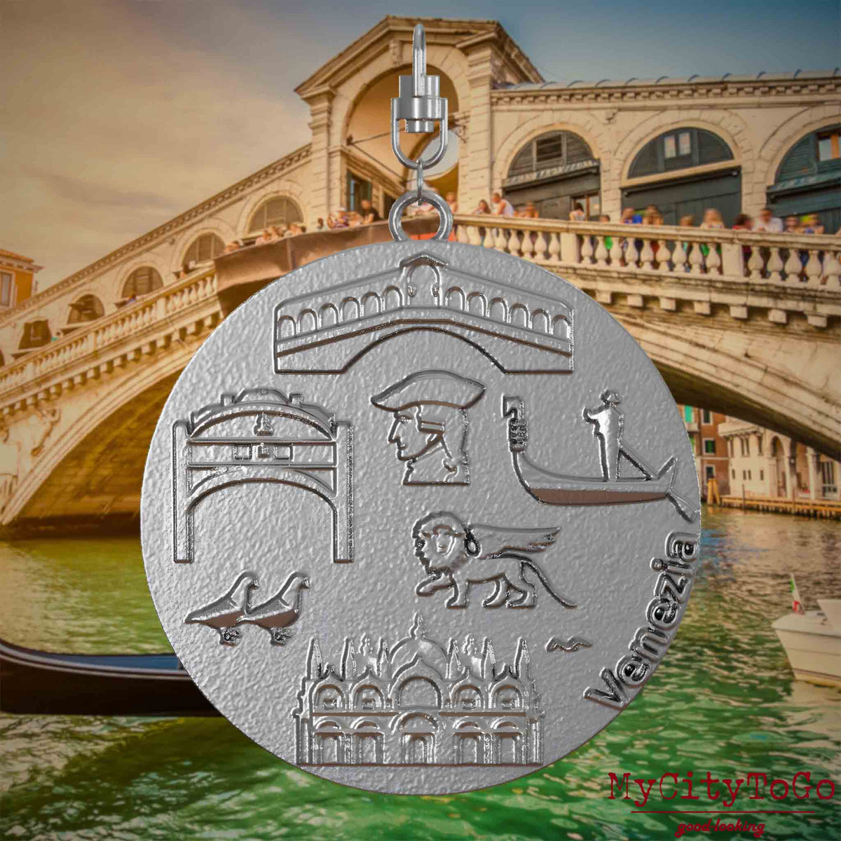 Halskette mit Drehwirbel und Vorderseite eines Schmuckanhängers aus Edelstahl, auf dem Reliefs bekannter Sehenswürdigkeiten der Stadt Venedig abgebildet sind. Den Hintergrund bildet eine Ansicht der Stadt Venedig.
