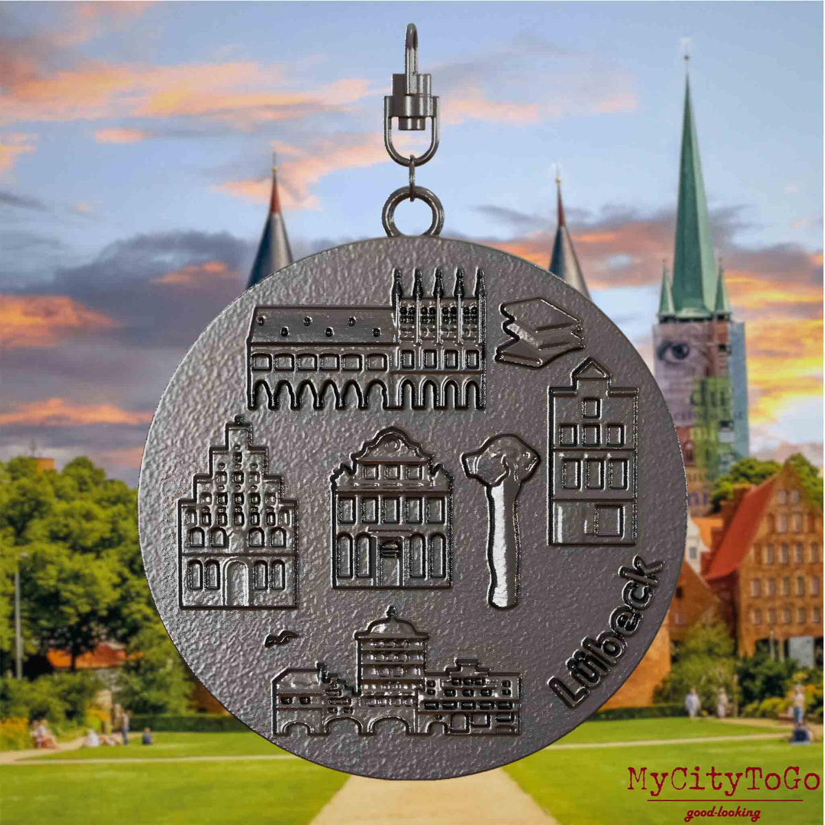 Halskette mit Drehwirbel und Vorderseite eines Schmuckanhängers aus Titan, auf dem Reliefs bekannter Sehenswürdigkeiten der Stadt Luebeck abgebildet sind. Den Hintergrund bildet eine Ansicht der Stadt Luebeck.
