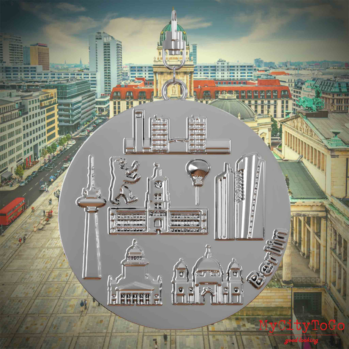 Halskette mit Drehwirbel und Vorderseite eines silbernen Schmuckanhängers, auf dem Reliefs bekannter Sehenswürdigkeiten der Stadt Berlin abgebildet sind. Den Hintergrund bildet eine Ansicht der Stadt Berlin.
