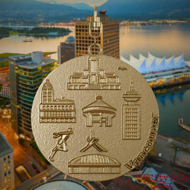 Halskette mit Drehwirbel und Rückseite eines Schmuckanhängers aus vergoldetem Edelstahl, auf dem Reliefs bekannter Sehenswürdigkeiten der Stadt Vancouver abgebildet sind. Den Hintergrund bildet eine Ansicht der Stadt Vancouver.
