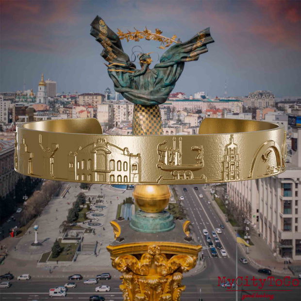 Armreif aus vergoldetem Edelstahl mit Reliefs bekannter Sehenswürdigkeiten der Stadt Kiew. Den Hintergrund bildet eine Ansicht der Stadt Kiew.
