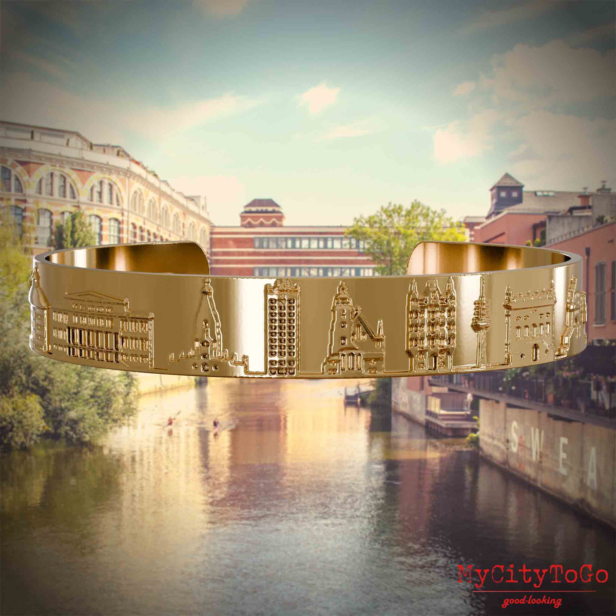 Vergoldeter Armreif mit Reliefs bekannter Sehenswürdigkeiten der Stad Leipzig. Den Hintergrund bildet eine Ansicht der Stadt Leipzig.