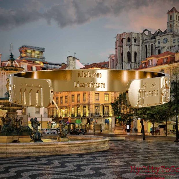 Innenseite eines vergoldeten Armreifs mit Reliefs bekannter Sehenswürdigkeiten der Stadt Lissabon und einer Gravur des Stadtnamens. Den Hintergrund bildet eine Ansicht der Stadt Lissabon.