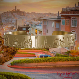 Armreif aus vergoldetem Edelstahl mit Reliefs bekannter Sehenswürdigkeiten der Stadt San Francisco. Den Hintergrund bildet eine Ansicht der Stadt San Francisco.