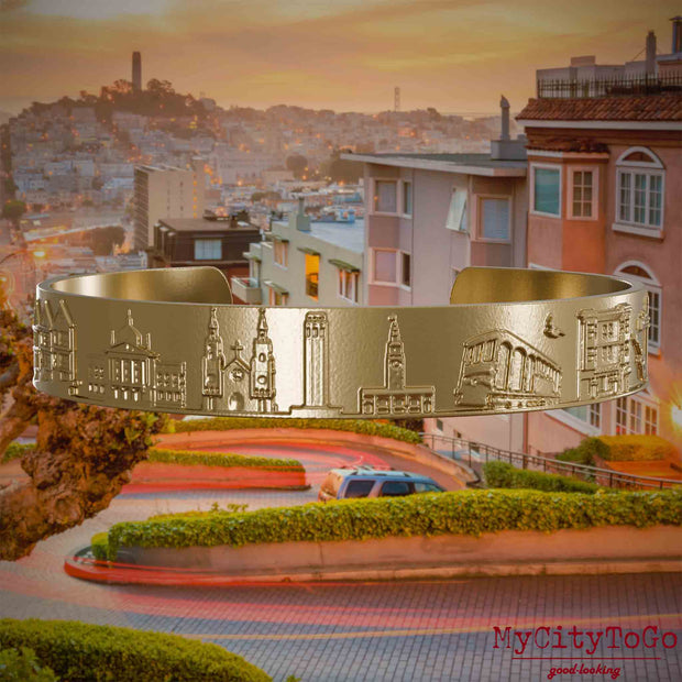 Armreif aus vergoldetem Edelstahl mit Reliefs bekannter Sehenswürdigkeiten der Stadt San Francisco. Den Hintergrund bildet eine Ansicht der Stadt San Francisco.