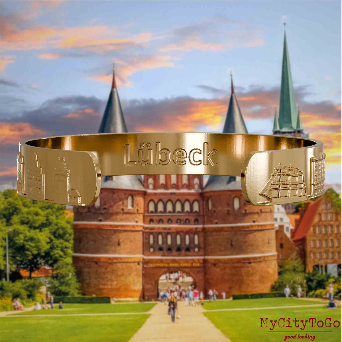 Innenseite eines vergoldeten Armreifs mit Reliefs bekannter Sehenswürdigkeiten der Stadt Luebeck und einer Gravur des Stadtnamens. Den Hintergrund bildet eine Ansicht der Stadt Luebeck.