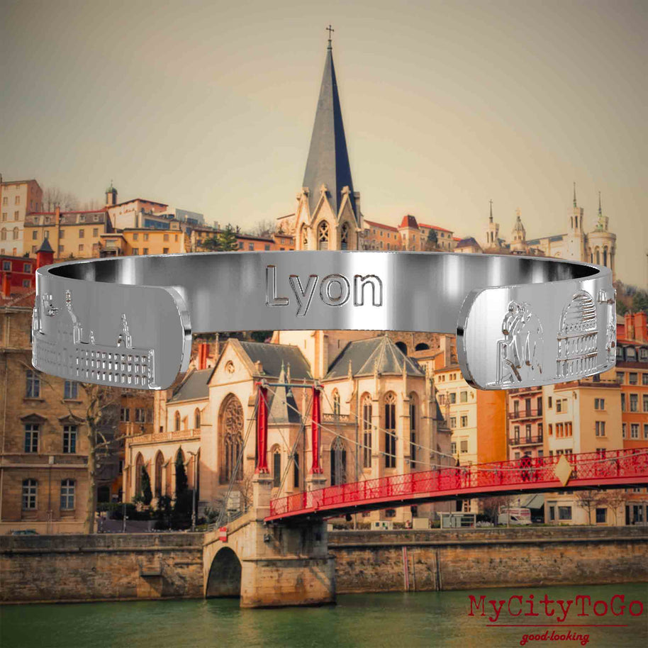 Innenseite eines silbernen Armreifs mit Reliefs bekannter Sehenswürdigkeiten der Stadt Lyon und einer Gravur des Stadtnamens. Den Hintergrund bildet eine Ansicht der Stadt Lyon.
