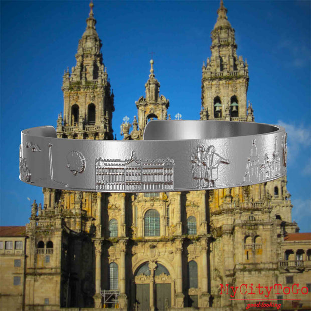 Armreif aus Edelstahl mit Reliefs bekannter Sehenswürdigkeiten und Elemente des Jakobsweges. Den Hintergrund bildet die Kathedrale von Santiago de Compostela.