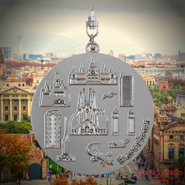 Halskette mit Drehwirbel und Rückseite eines silbernen Schmuckanhängers, auf dem Reliefs bekannter Sehenswürdigkeiten der Stadt Barcelona abgebildet sind. Den Hintergrund bildet eine Ansicht der Stadt Barcelona.
