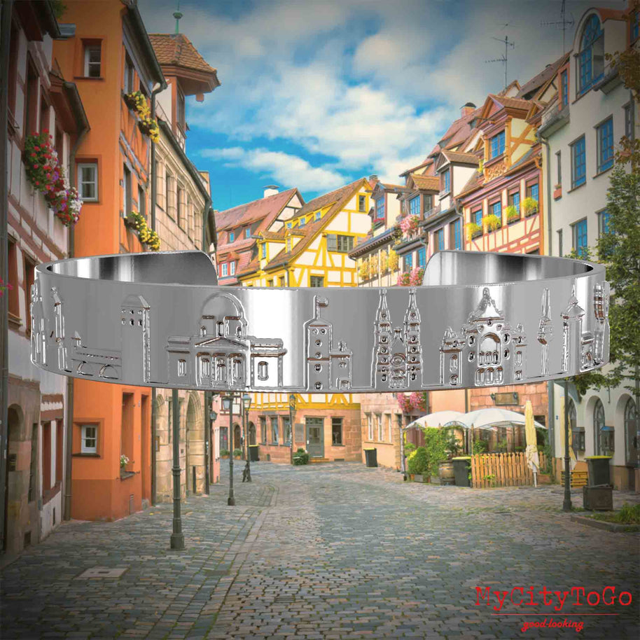 Versilberter Armreif mit Reliefs bekannter Sehenswürdigkeiten der Stadt Nürnberg. Den Hintergrund bildet eine Ansicht der Stadt  Nuernberg.