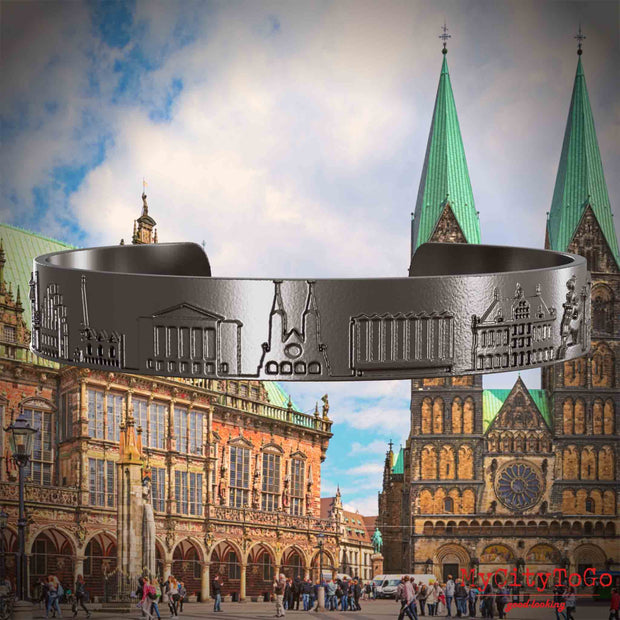 Armreif aus Titan mit Reliefs bekannter Sehenswürdigkeiten der Stadt Bremen. Den Hintergrund bildet eine Ansicht der Stadt Bremen.
