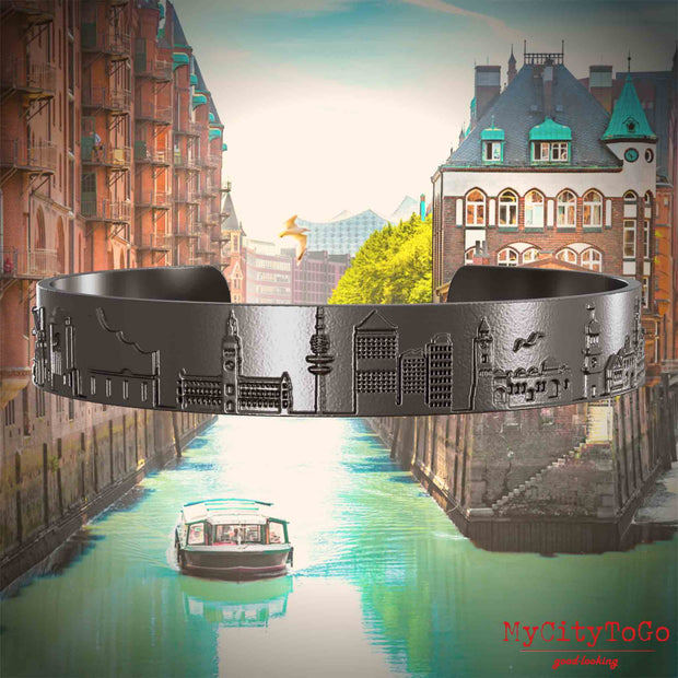 Armreif aus Titan mit Reliefs bekannter Sehenswürdigkeiten der Stadt Hamburg. Den Hintergrund bildet eine Ansicht der Stadt Hamburg.