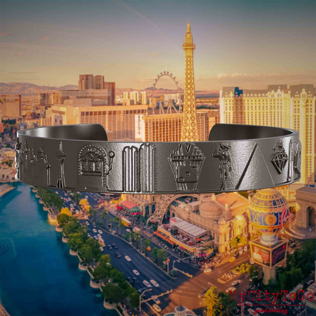 Armreif aus Titan mit Reliefs bekannter Sehenswürdigkeiten der Stadt Las Vegas. Den Hintergrund bildet eine Ansicht der Stadt Las Vegas.