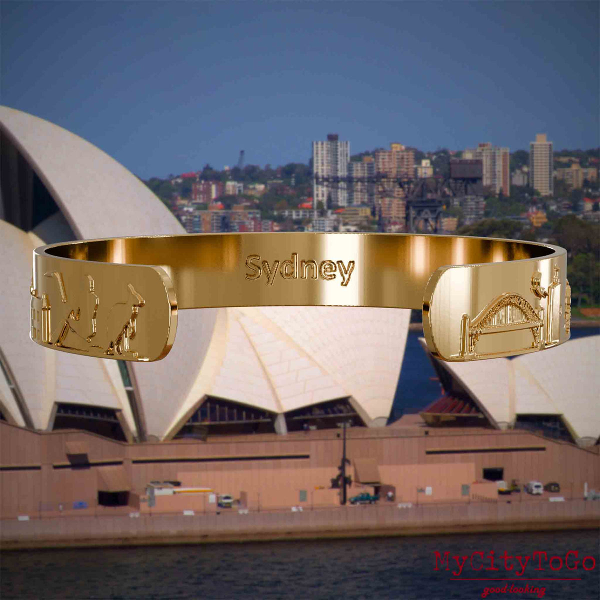Innenseite eines vergoldeten Armreifs mit Reliefs bekannter Sehenswürdigkeiten der Stadt Sydney und einer Gravur des Stadtnamens . Den Hintergrund bildet eine Ansicht der Stadt Sydney.