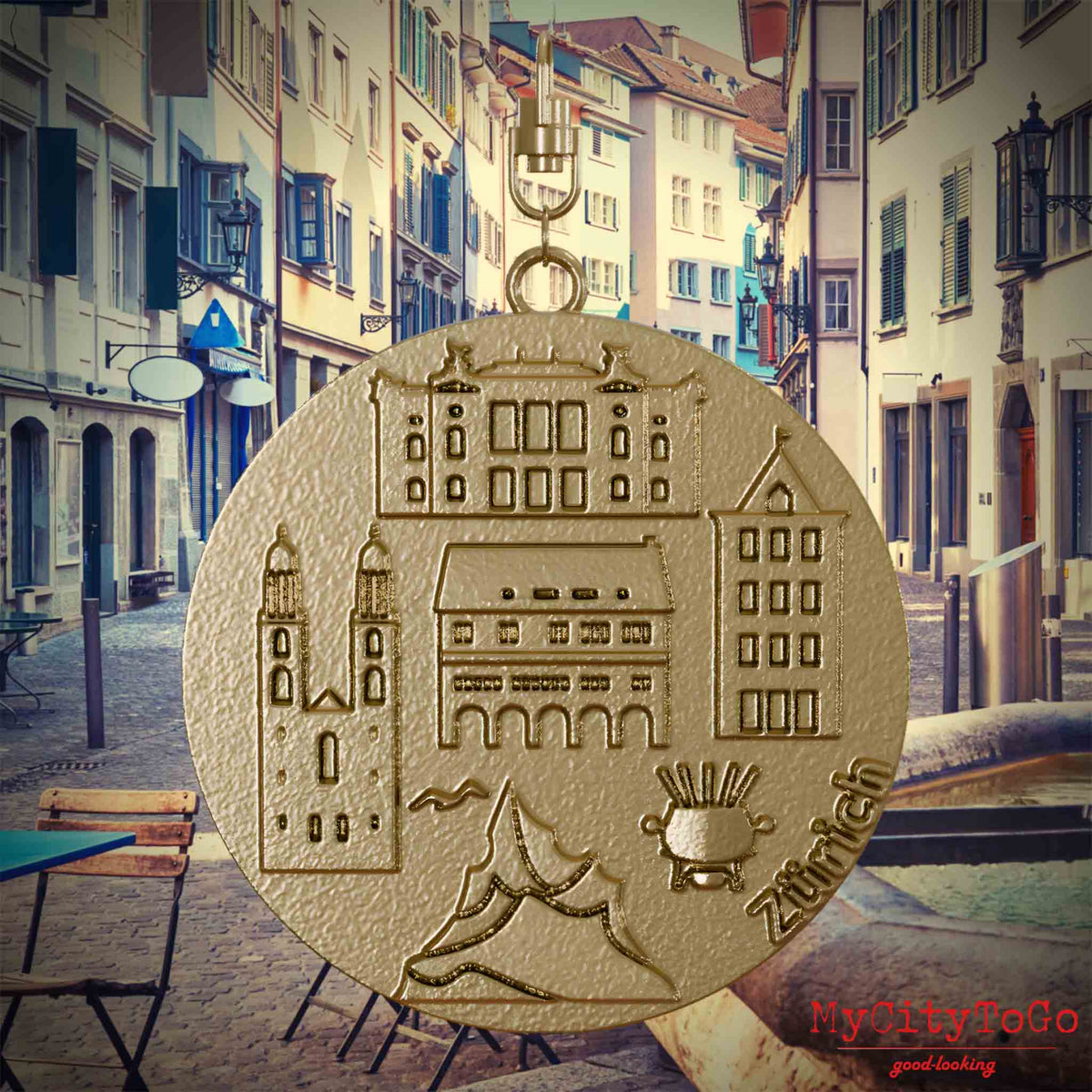 Halskette mit Drehwirbel und Vorderseite eines Schmuckanhängers aus vergoldetem Edelstahl, auf dem Reliefs bekannter Sehenswürdigkeiten der Stadt Zuerich abgebildet sind. Den Hintergrund bildet eine Ansicht der Stadt Zuerich.
