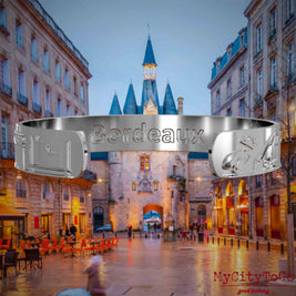 Innenseite eines silbernen Armreifs mit Reliefs bekannter Sehenswürdigkeiten der Stadt Bordeaux und einer Gravur des Stadtnamens. Den Hintergrund bildet eine Ansicht der Stadt Bordeaux.