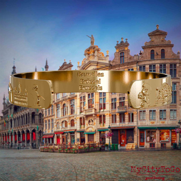 Innenseite eines vergoldeten Armreifs mit Reliefs bekannter Sehenswürdigkeiten der Stadt Brüssel und einer Gravur des Stadtnamens. Den Hintergrund bildet eine Ansicht der Stadt Bruessel.