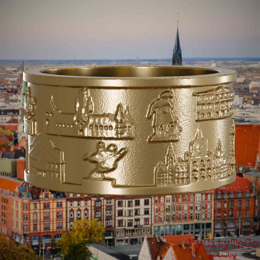 Ring aus vergoldetem Edelstahl mit Reliefs bekannter Sehenswürdigkeiten der Stadt Hannover. Den Hintergrund bildet eine Ansicht der Stadt Hannover.