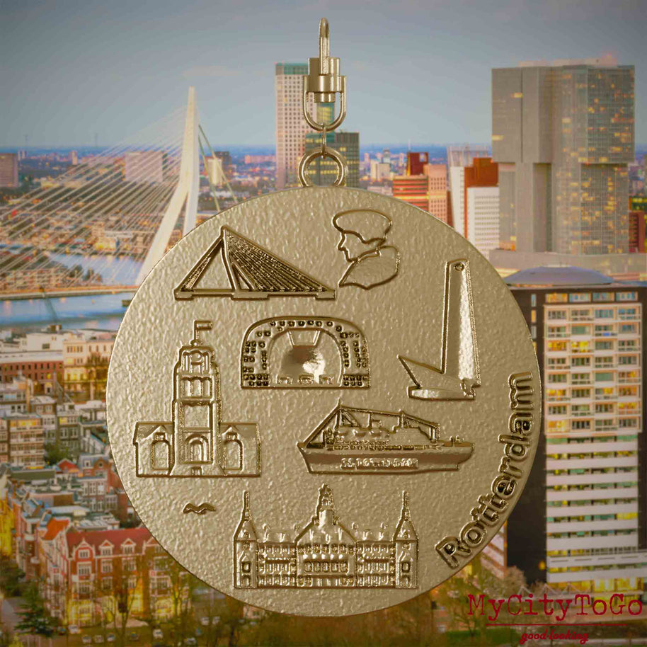Halskette mit Drehwirbel und Rückseite eines Schmuckanhängers aus vergoldetem Edelstahl, auf dem Reliefs bekannter Sehenswürdigkeiten der Stadt Rotterdam abgebildet sind. Den Hintergrund bildet eine Ansicht der Stadt Rotterdam.
