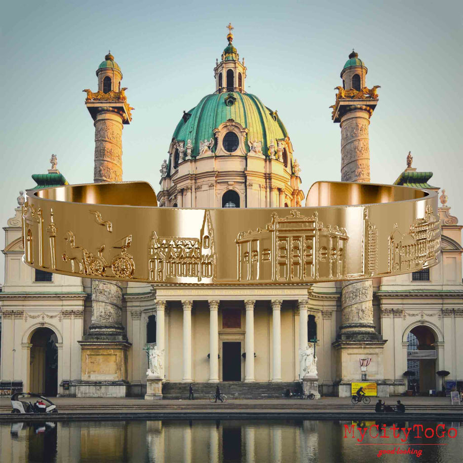 Vergoldeter Armreif mit Reliefs bekannter Sehenswürdigkeiten der Stadt Wien. Den Hintergrund bildet eine Ansicht der Stadt Wien.