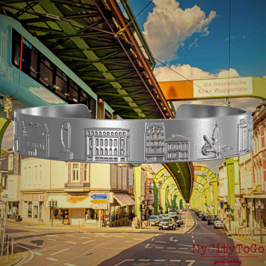 Armreif aus Edelstahl mit Reliefs bekannter Sehenswürdigkeiten der Stadt Wupertal. Den Hintergrund bildet eine Ansicht  der Stadt Wuppertal.