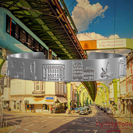 Armreif aus Edelstahl mit Reliefs bekannter Sehenswürdigkeiten der Stadt Wupertal. Den Hintergrund bildet eine Ansicht  der Stadt Wuppertal.