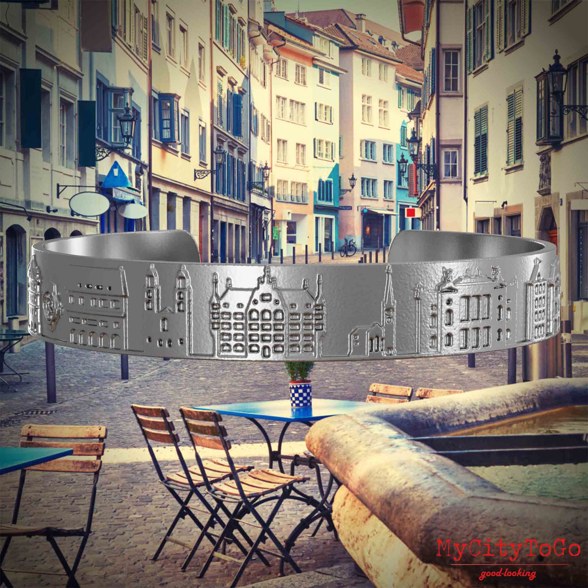 Armreif aus Edelstahl mit Reliefs bekannter Sehenswürdigkeiten der Stadt Zuerich. Den Hintergrund bildet eine Ansicht der Stadt Zuerich.