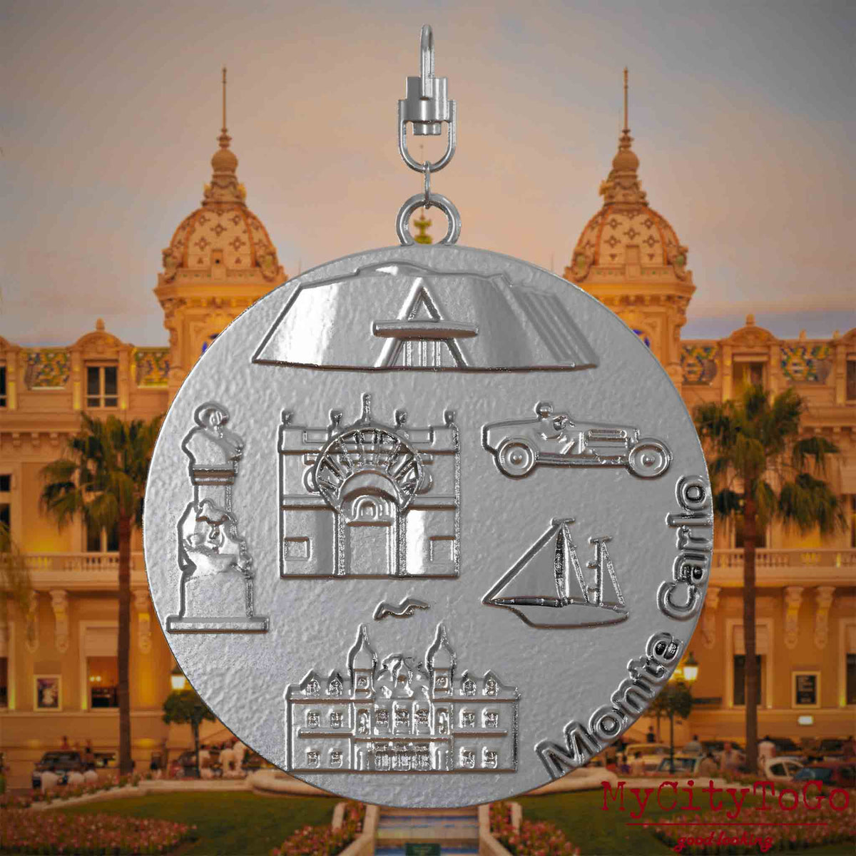 Halskette mit Drehwirbel und Vorderseite eines Schmuckanhängers aus Edelstahl, auf dem Reliefs bekannter Sehenswürdigkeiten der Stadt Monte Carlo abgebildet sind. Den Hintergrund bildet eine Ansicht der Stadt Monte Carlo.
