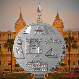 Halskette mit Drehwirbel und Vorderseite eines Schmuckanhängers aus Edelstahl, auf dem Reliefs bekannter Sehenswürdigkeiten der Stadt Monte Carlo abgebildet sind. Den Hintergrund bildet eine Ansicht der Stadt Monte Carlo.
