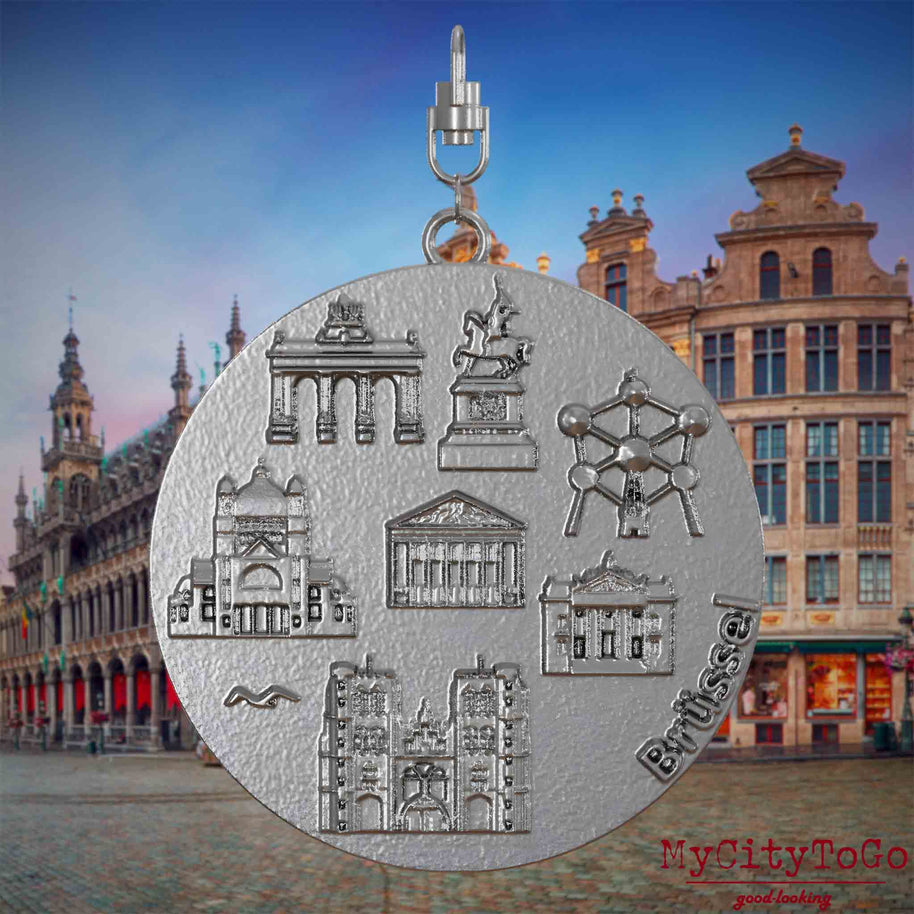 Halskette mit Drehwirbel und Rückseite eines Schmuckanhängers aus Edelstahl, auf dem Reliefs bekannter Sehenswürdigkeiten der Stadt Bruessel abgebildet sind. Den Hintergrund bildet eine Ansicht der Stadt Bruessel.
