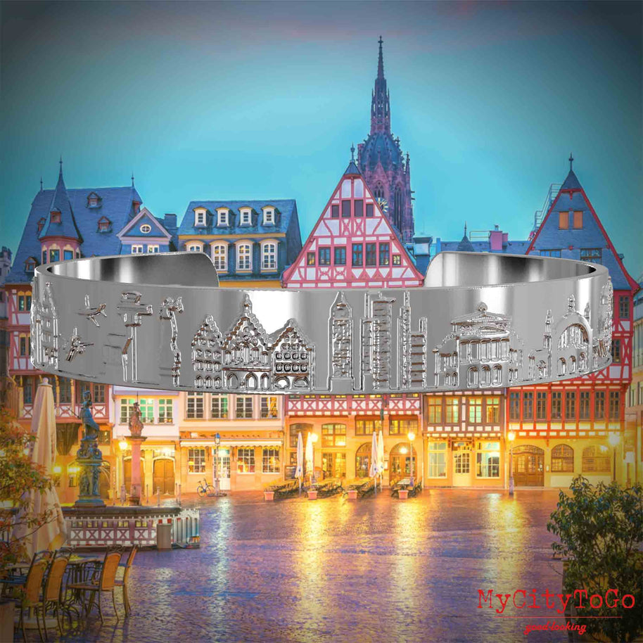 Versilberter Armreif mit Reliefs bekannter Sehenswürdigkeiten der Stadt Frankfurt. Den Hintergrund bildet eine Ansicht der Stadt Frankfurt.