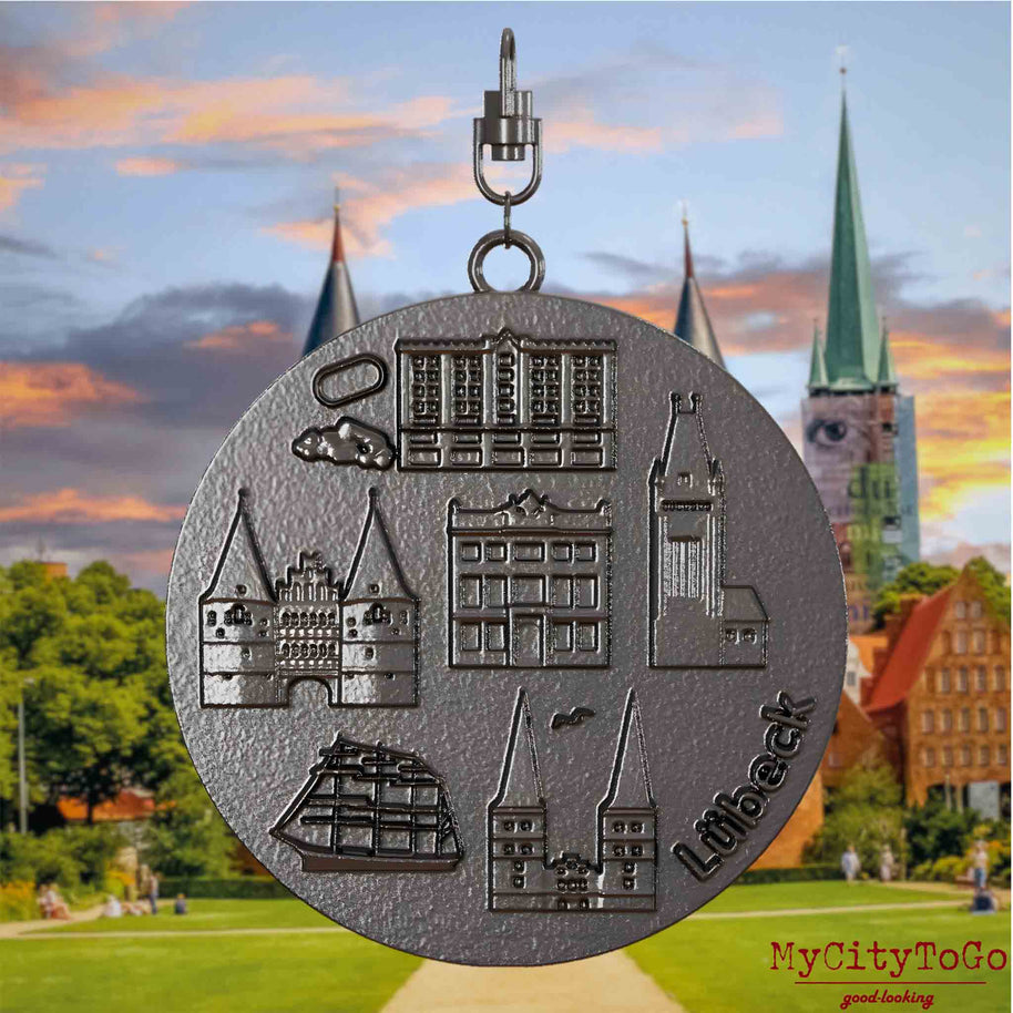 Halskette mit Drehwirbel und Rückseite eines Schmuckanhängers aus Titan, auf dem Reliefs bekannter Sehenswürdigkeiten der Stadt Luebeck abgebildet sind. Den Hintergrund bildet eine Ansicht der Stadt Luebeck.
