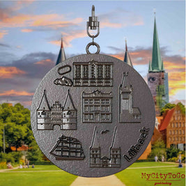 Halskette mit Drehwirbel und Rückseite eines Schmuckanhängers aus Titan, auf dem Reliefs bekannter Sehenswürdigkeiten der Stadt Luebeck abgebildet sind. Den Hintergrund bildet eine Ansicht der Stadt Luebeck.
