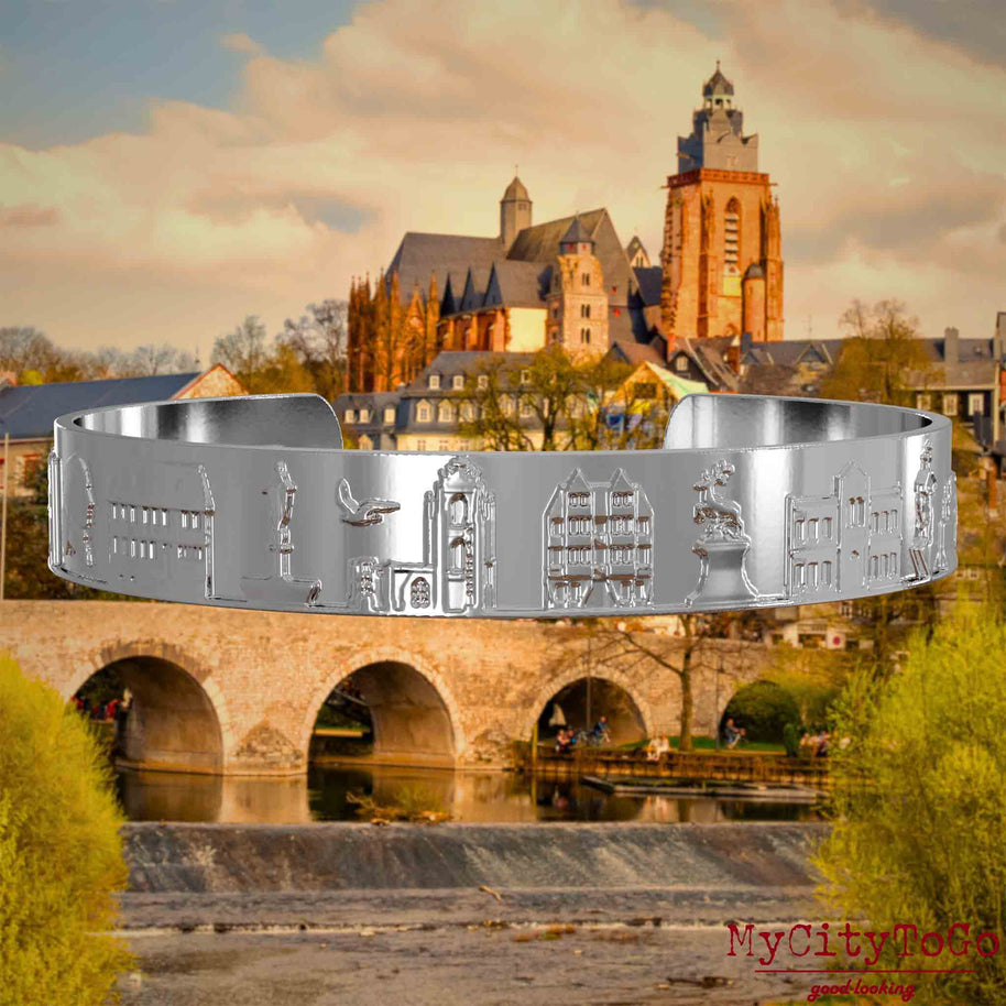 Versilberter Armreif mit Reliefs bekannter Sehenswürdigkeiten der Stadt Wetzlar. Den Hintergrund bildet eine Ansicht der Stadt Wetzlar.
